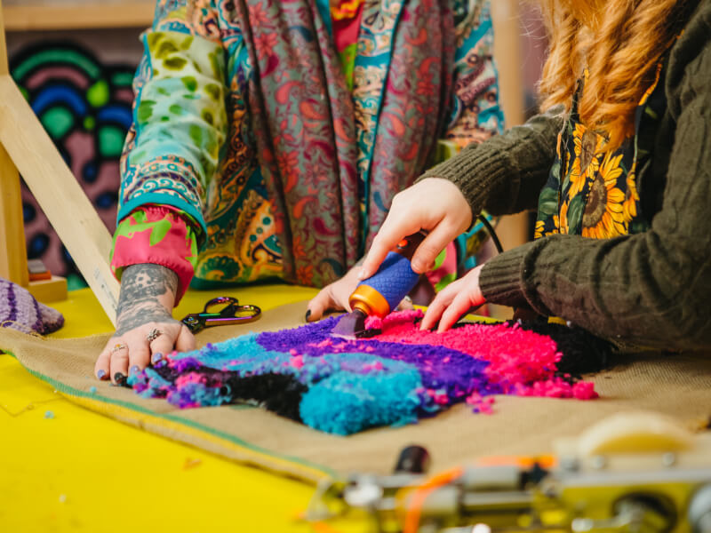 Two colourfully-dressed people making a tufted rug together